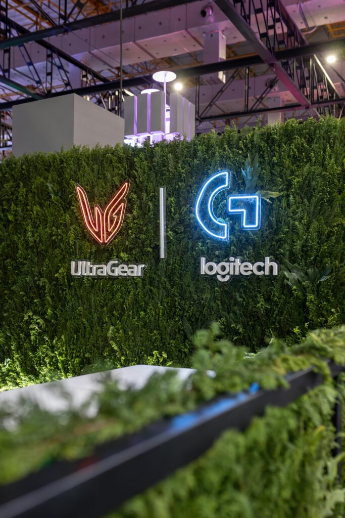 Lush greenery wall with illuminated UltraGear and Logitech logos at indoor exhibition.